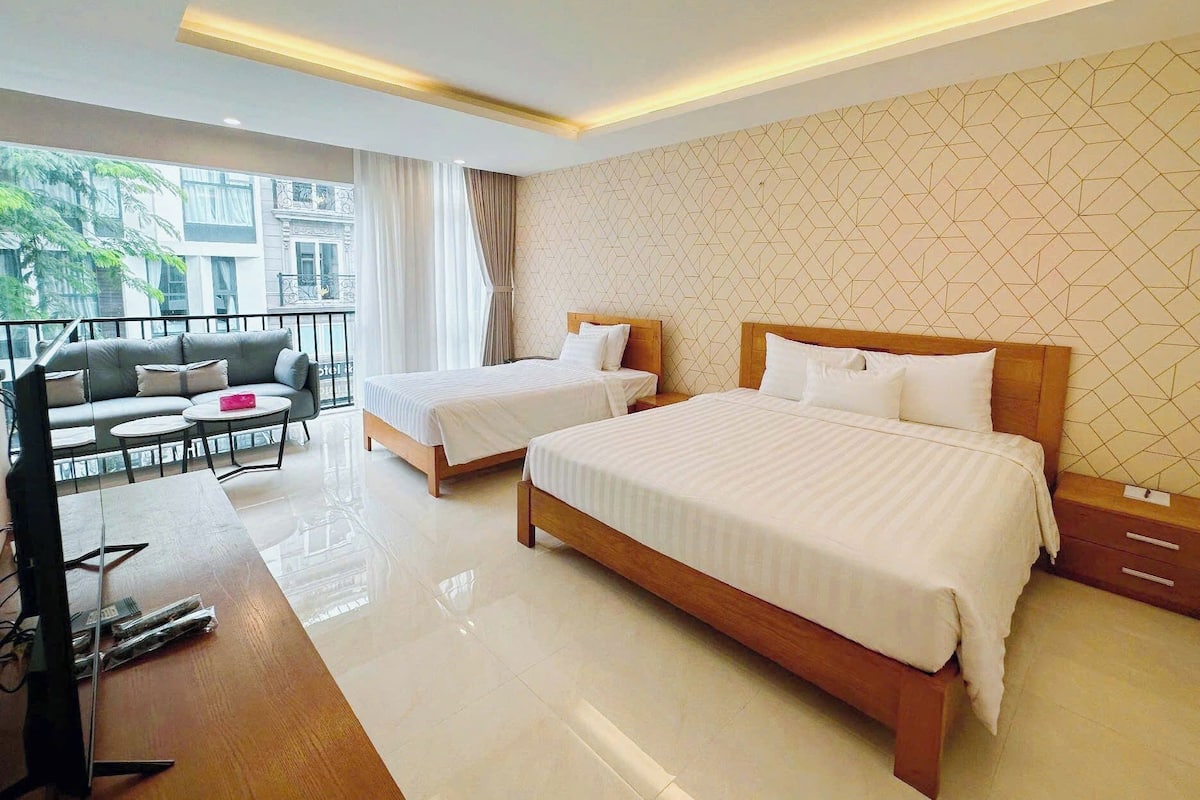 Quarto de hotel com duas camas, um sofá, uma mesa pequena e varanda com vista.