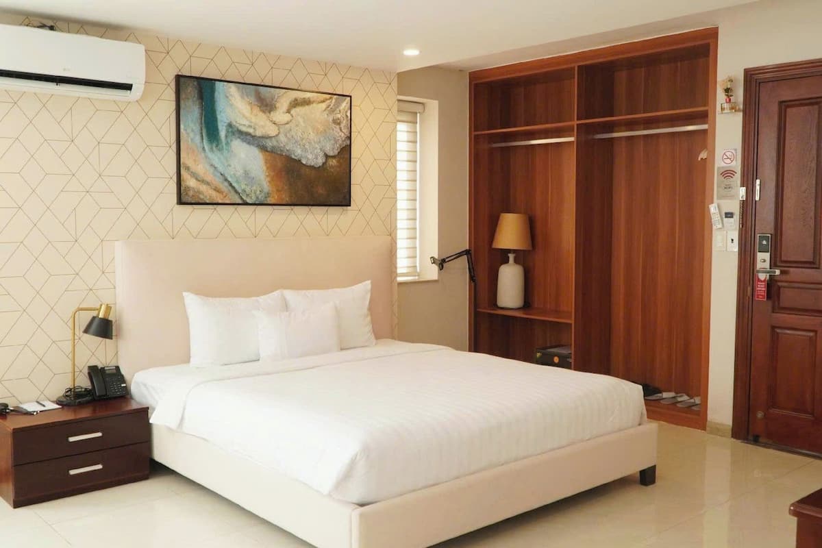 Um quarto com cama, luminária de cabeceira, mesa de cabeceira e um guarda-roupa de madeira.