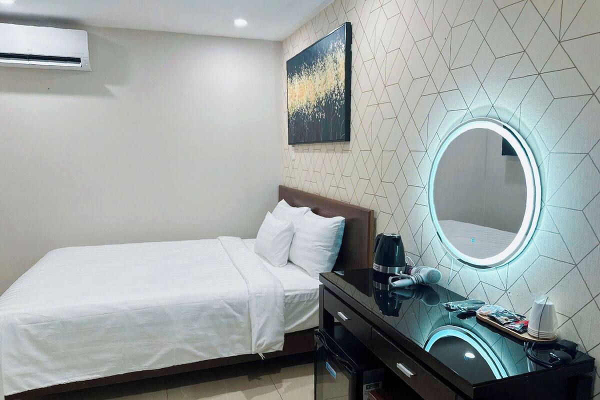 Quarto de hotel com cama, escrivaninha com espelho, cafeteira e ar condicionado fixado na parede.
