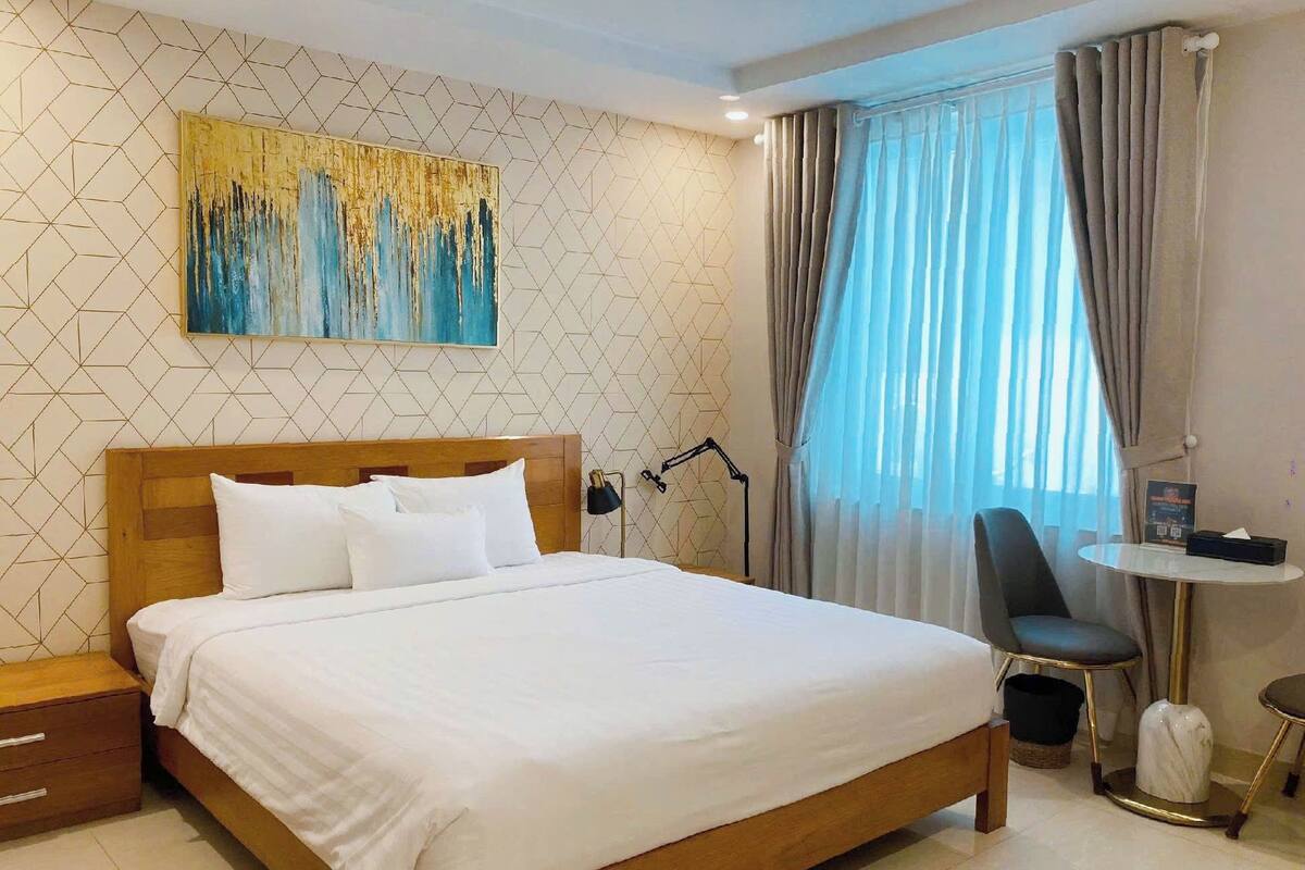 Quarto de hotel com cama de madeira, escrivaninha com cadeira, abajur e pintura na parede.