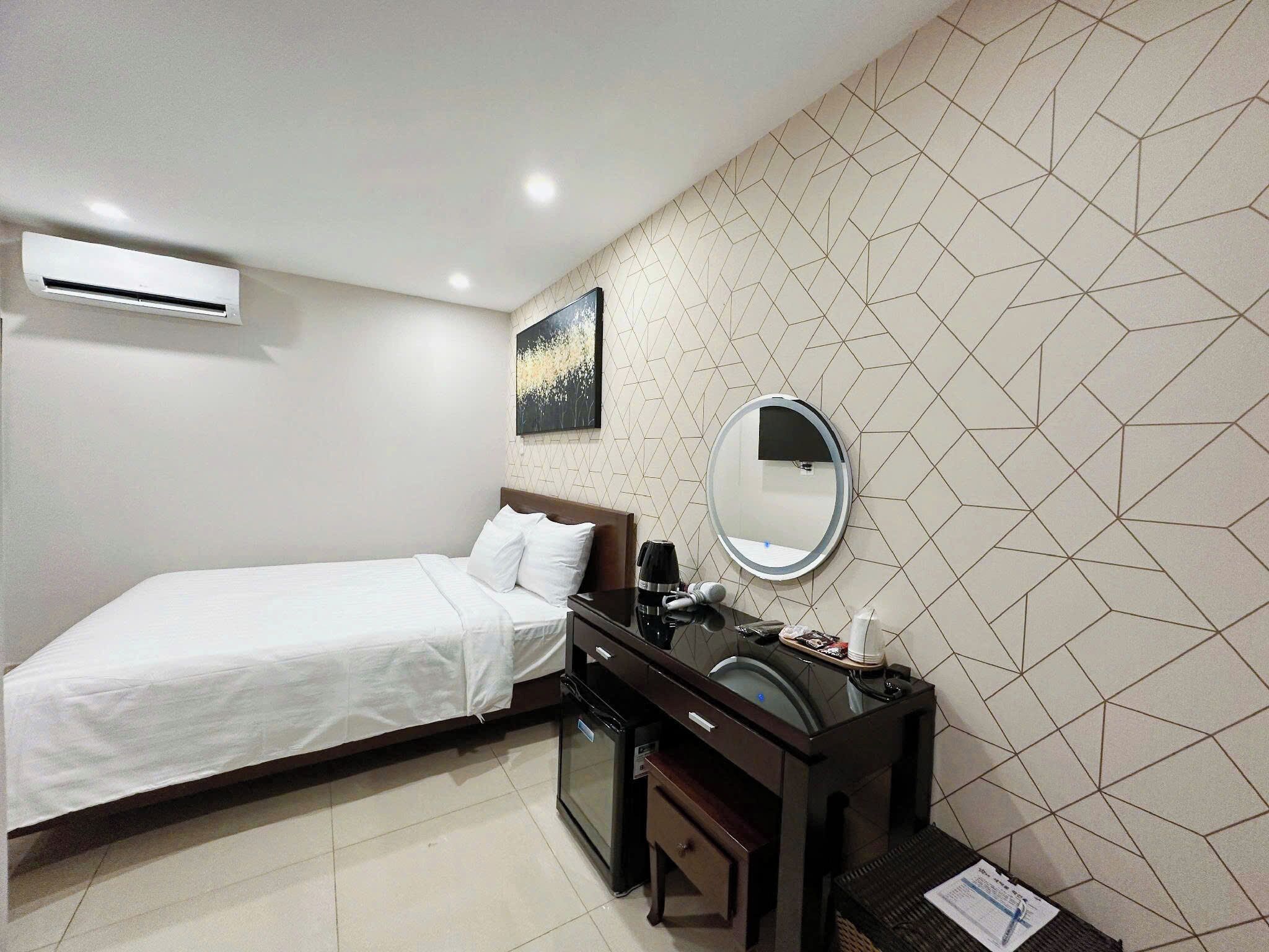 Une chambre d’hôtel avec un lit, une coiffeuse avec un miroir et un mur orné d’un motif géométrique.
