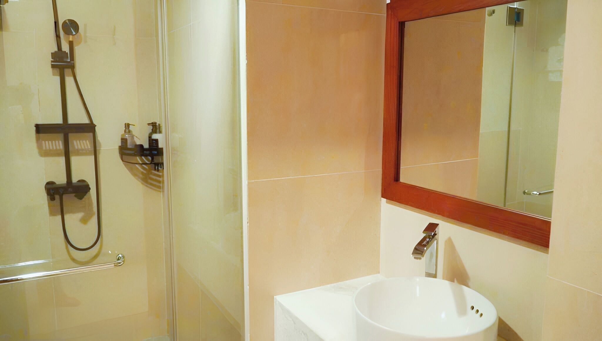 Un baño con cabina de ducha de vidrio, un lavamanos blanco y un espejo con marco de madera.