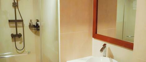 Un baño con cabina de ducha de vidrio, un lavamanos blanco y un espejo con marco de madera.