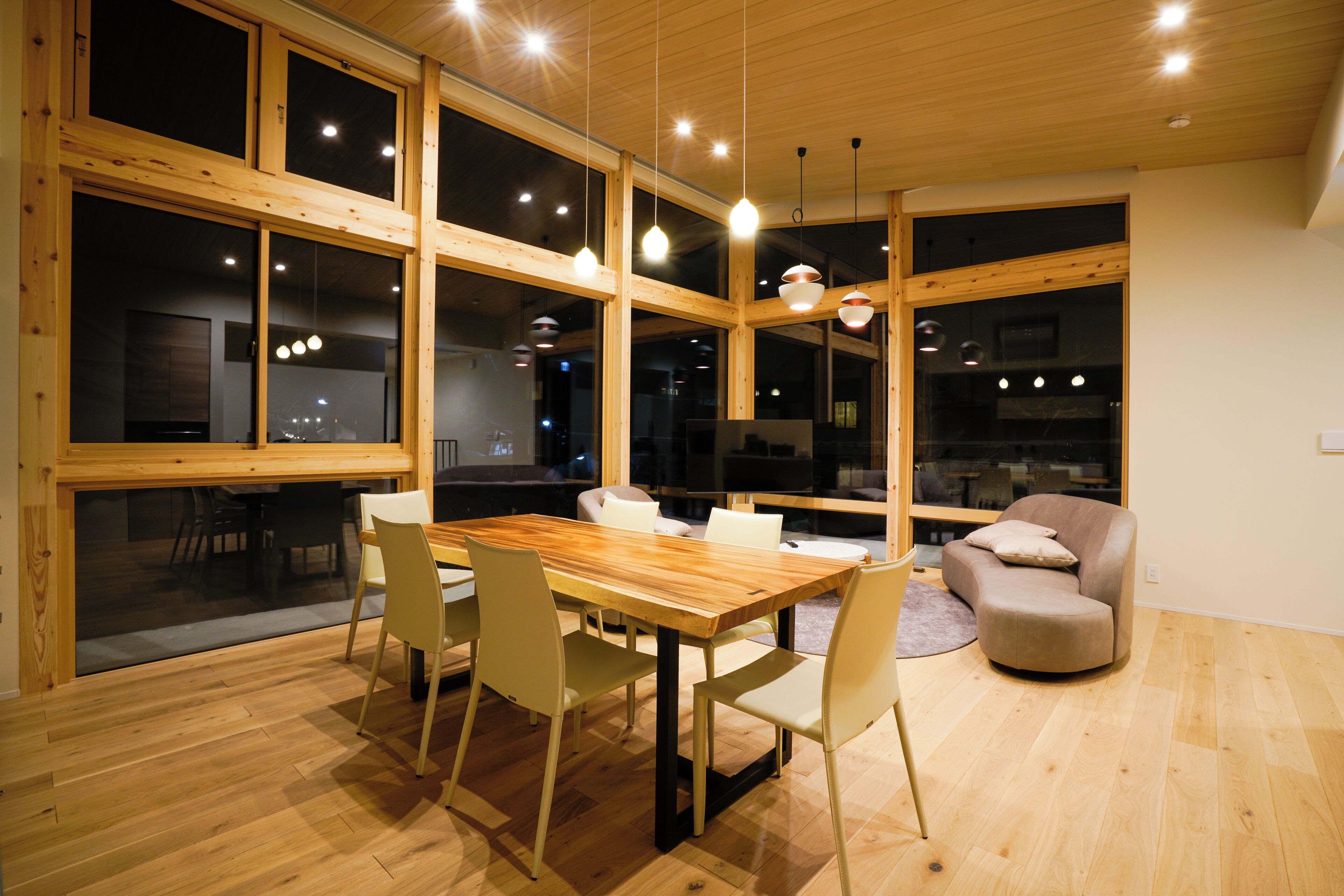 A modern dining area with a wooden table and chairs, large windows, and pendant lighting.