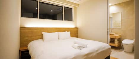 Camera d'albergo con un letto grande, una testiera in legno, una finestra, un bagno con lavandino e WC, e uno specchio.