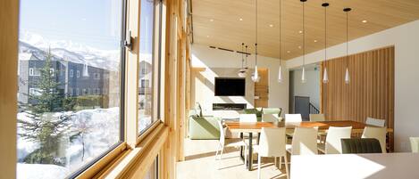 Un interior moderno con comedor, cocina y amplios ventanales con vistas a montañas nevadas.