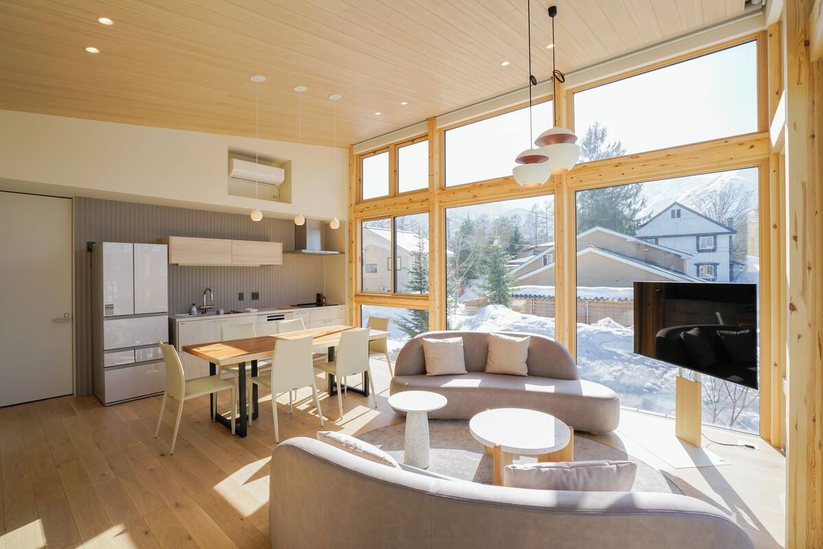 A modern interior with a kitchen, dining area, and living space with large windows and a view of a snowy landscape.