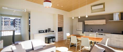 Een moderne woonkamer met een bank, salontafel en een eethoek met stoelen. Er is een keuken met een fornuis, magnetron en kasten.