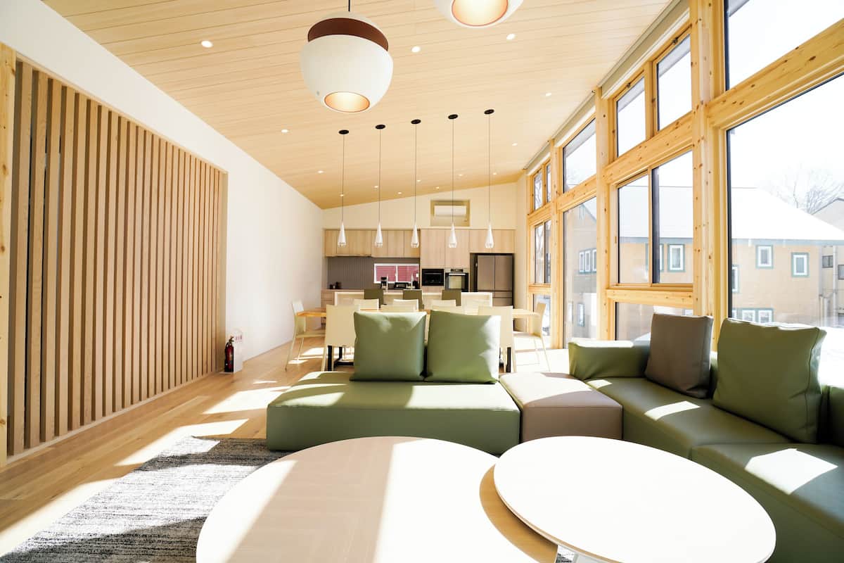 A modern living room with a large window, a sofa, a coffee table, and a kitchen in the background.