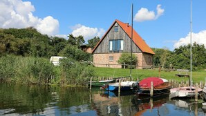 Une maison de campagne en bois, avec un toit rouge, entourée d’un lac paisible où sont amarrés des bateaux.