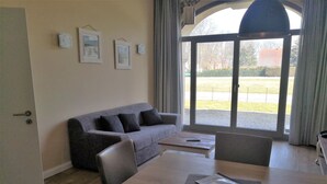 Un salon moderne avec un canapé gris, une table à manger en bois et une vue dégagée grâce à de grandes portes vitrées.