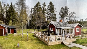 A cabin with a deck, surrounded by a forest.