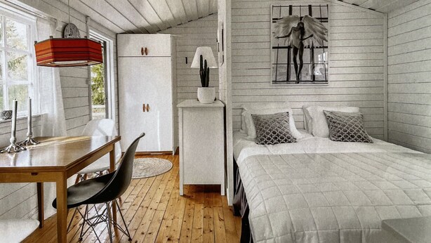 A bedroom with a bed, a desk, a chair, a lamp, and a wall-mounted artwork.