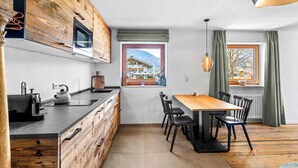A modern kitchen with wooden cabinetry, a wooden dining table, and black chairs. - Studio Bairerkopf | Pool, sauna & mountain view (Reit im Winkl)