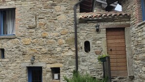 Un bâtiment en pierre avec une porte bleue, une petite fenêtre et une porte en bois. Des plantes se trouvent devant le bâtiment.