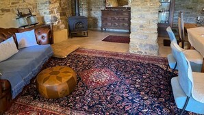 Une pièce chaleureuse avec un mur en pierre, une cheminée, un canapé, un tapis à motifs et une commode en bois.
