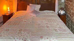 Une chambre avec un mur en pierre, un lit en bois doté d’un baldaquin et une table de chevet avec une lampe.