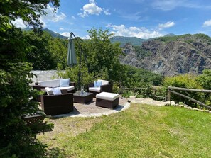 Een terras met rieten meubilair en een tafel, omgeven door groen en een bergachtig landschap.