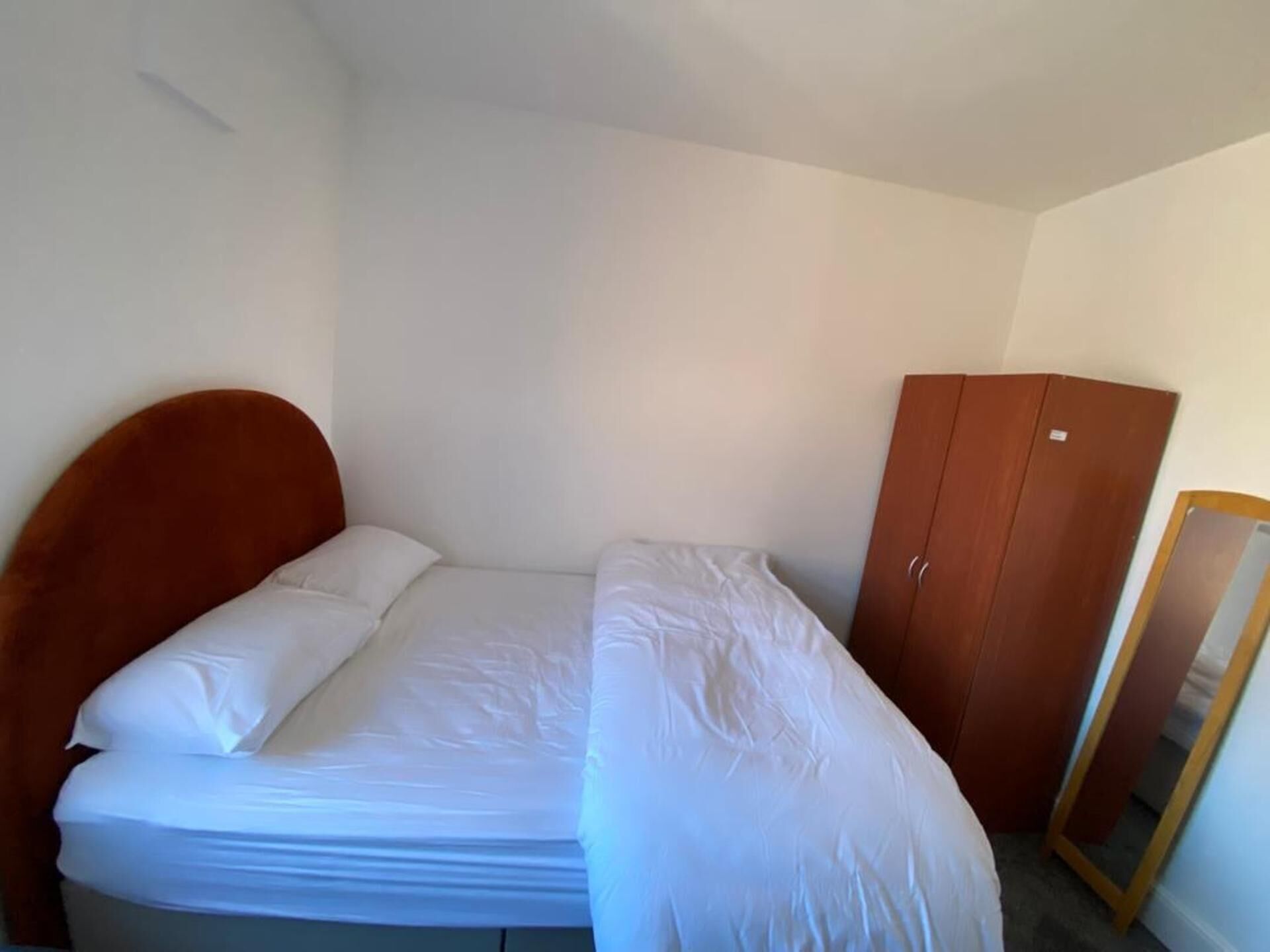 A small, single-bed room with a wooden headboard, a wooden wardrobe, and a mirror.