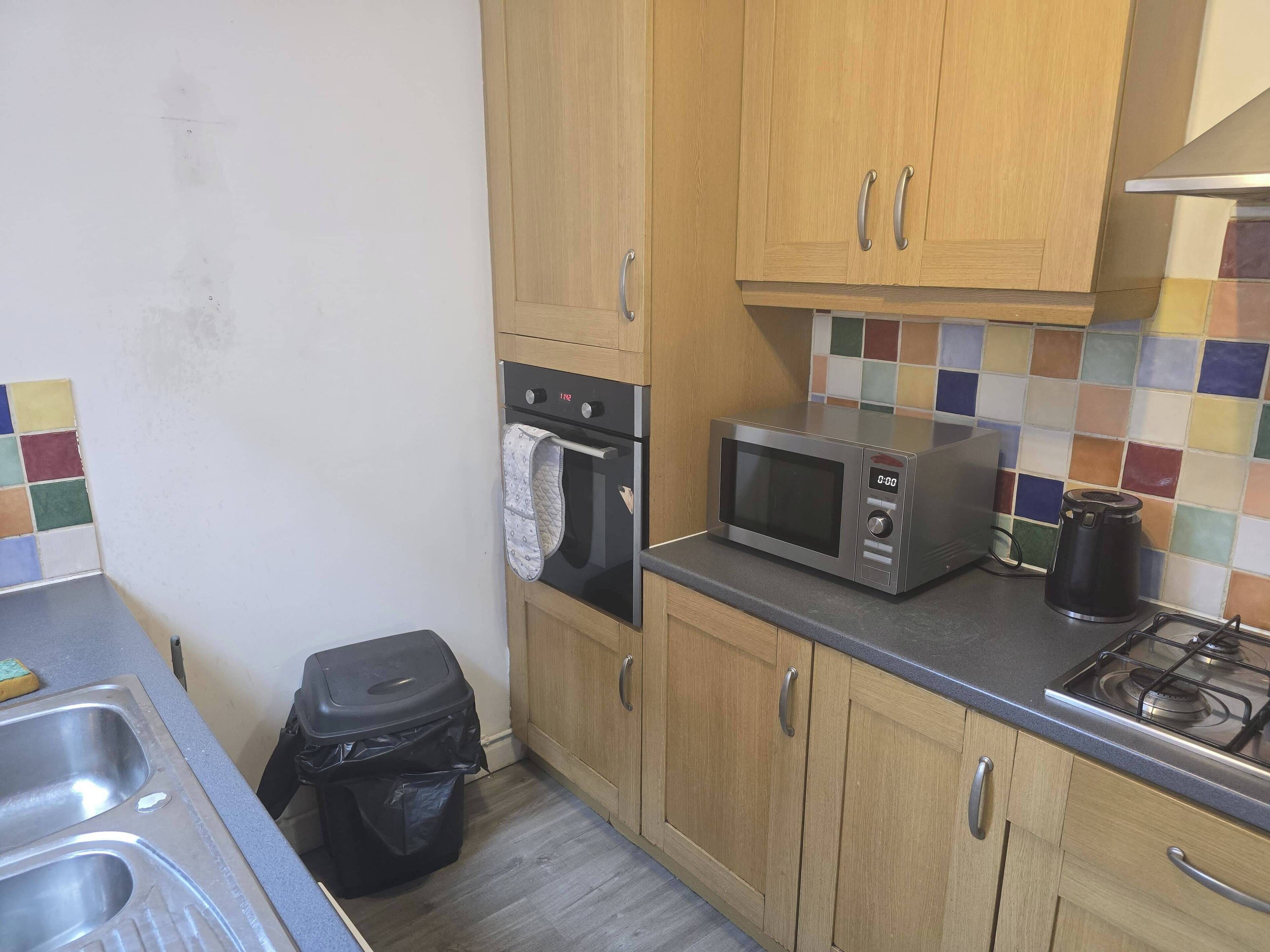 A compact kitchen with wooden cabinets, a microwave, a stove, and a tiled backsplash.
