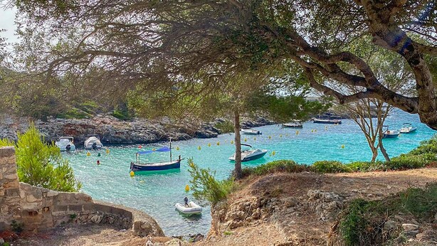 A coastal scene with boats anchored in clear blue waters, surrounded by rocky terrain and sparse vegetation. - My Rental Homes - Villa Neper with private pool, terrace and covered parking (Sant Lluís)