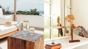 A balcony with a view of the sea, a wooden table with glasses and a water bottle, and a decorative wooden sculpture. - My Rental Homes - Villa Neper with private pool, terrace and covered parking (Sant Lluís)