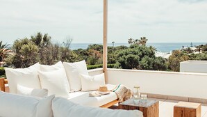 A balcony with a white sofa, a wooden table with glasses, and a view of the sea and greenery. - My Rental Homes - Villa Neper with private pool, terrace and covered parking (Sant Lluís)