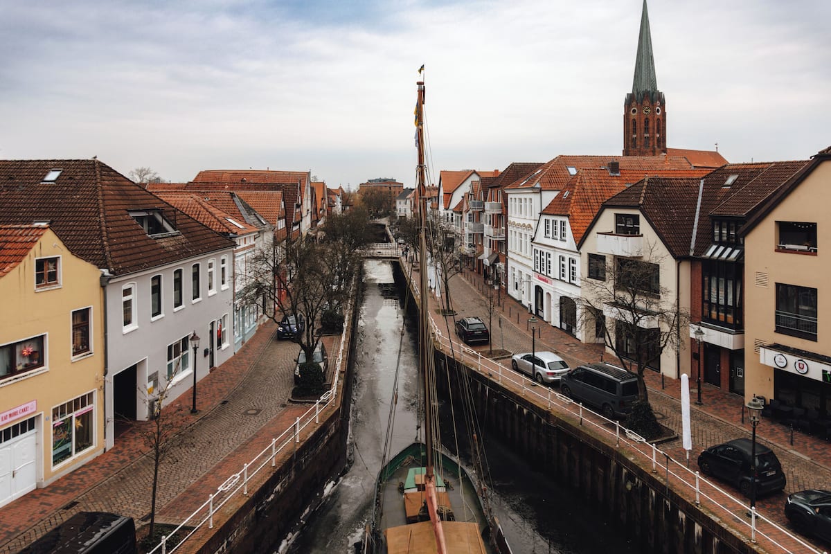 A canal with buildings on either side, a bridge, and a church spire in the distance.