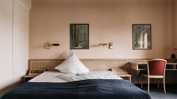 Habitación de hotel con una cama, un escritorio, una silla y dos cuadros en la pared.