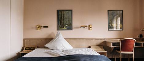 Une chambre d’hôtel avec un lit, un bureau, une chaise et deux tableaux encadrés au mur.