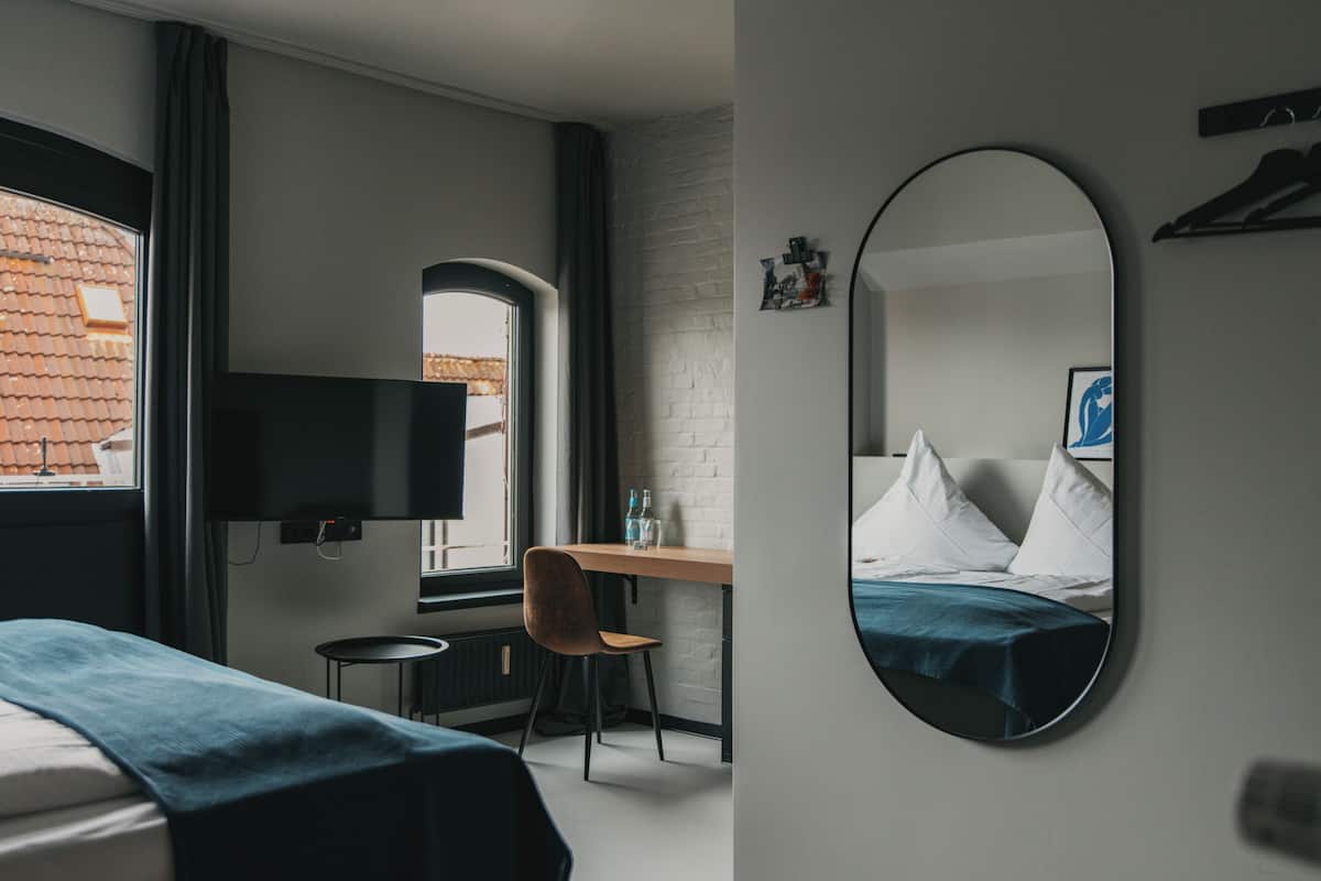 A hotel room with a bed, a desk with a chair, a television, and a large mirror.