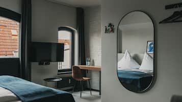 A hotel room with a bed, a desk with a chair, a television, and a large mirror.