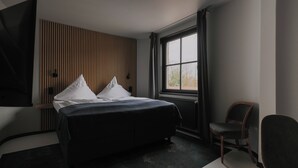 Una habitación de hotel moderna con una cama grande, una silla, una ventana con cortinas y un televisor montado en la pared.
