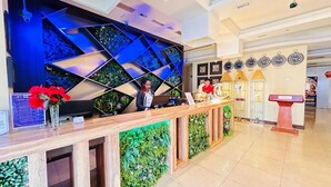Een receptiegedeelte met een modern design, met een houten receptiebalie, een digitaal scherm en een wand met geometrische patronen en begroening.