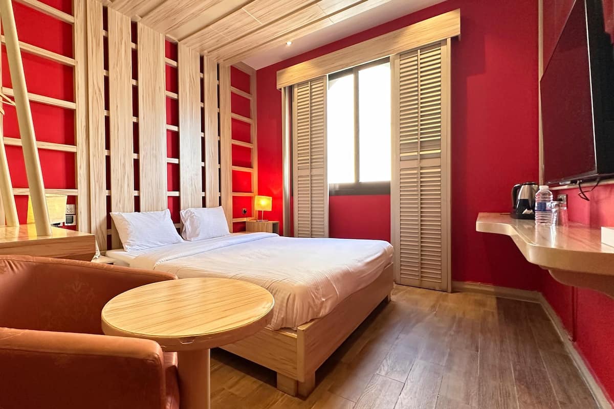 Un dormitorio con cama, una silla, una mesita, un televisor y una ventana con contraventanas.