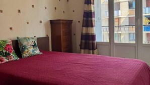 A bedroom with a red bedspread, a wooden dresser, and a curtain. - Escapade Provençale downtown (Saint-Raphaël)