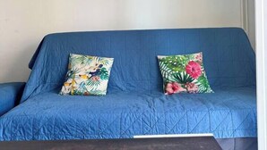 A blue sofa with floral cushions, a framed landscape painting on the wall, and a dark wooden table in the foreground. - Escapade Provençale downtown (Saint-Raphaël)