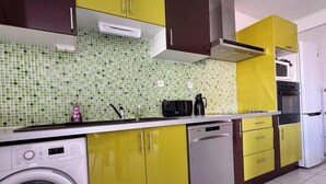 A kitchen with yellow and brown cabinets, a washing machine, a dishwasher, and a microwave. - Escapade Provençale downtown (Saint-Raphaël)