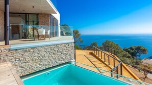 A modern house with a stone exterior, a glass balcony, and a pool. - My Rental Homes | Villa Mirante  with sea view and private pool (Begur)