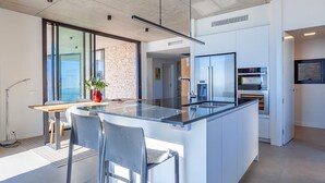 A modern kitchen with a large island, built-in appliances, and a view to the living area. - My Rental Homes | Villa Mirante  with sea view and private pool (Begur)