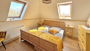 A bedroom with a large bed, two bedside tables, a radiator, a window, and a hanging light fixture. - Eckhorst Farm, Landtraum (Güby)