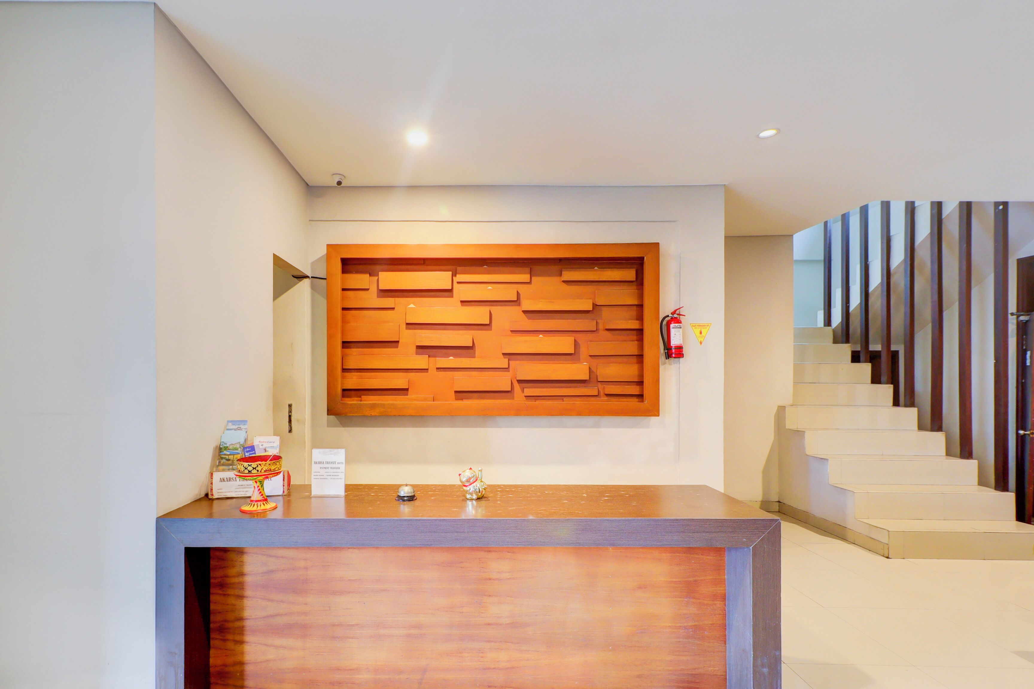 A reception desk with a wooden panel design, a staircase with wooden railings, and a fire extinguisher mounted on the wall.