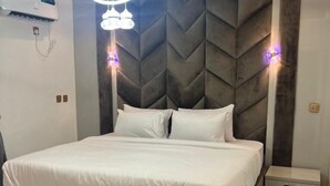 A modern bedroom with a large bed, a headboard with a geometric pattern, and bedside lamps. - Fina Shortlet Apartment  (Abuja)