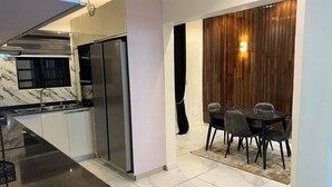 A modern kitchen with stainless steel appliances, a marble backsplash, and a dining area with a dark table and chairs. - Fina Shortlet Apartment  (Abuja)