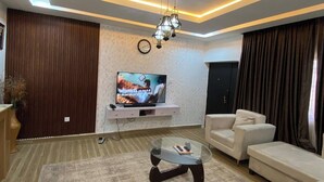 A modern living room with a flat-screen TV, a glass coffee table, and a sofa. - Fina Shortlet Apartment  (Abuja)