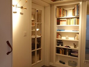 A corner of a room with a white bookshelf filled with books and a glass-fronted cabinet.