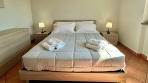 Una cama bien tendida con sábanas y toallas blancas, dos mesitas de noche con lámparas y un cabecero de madera.