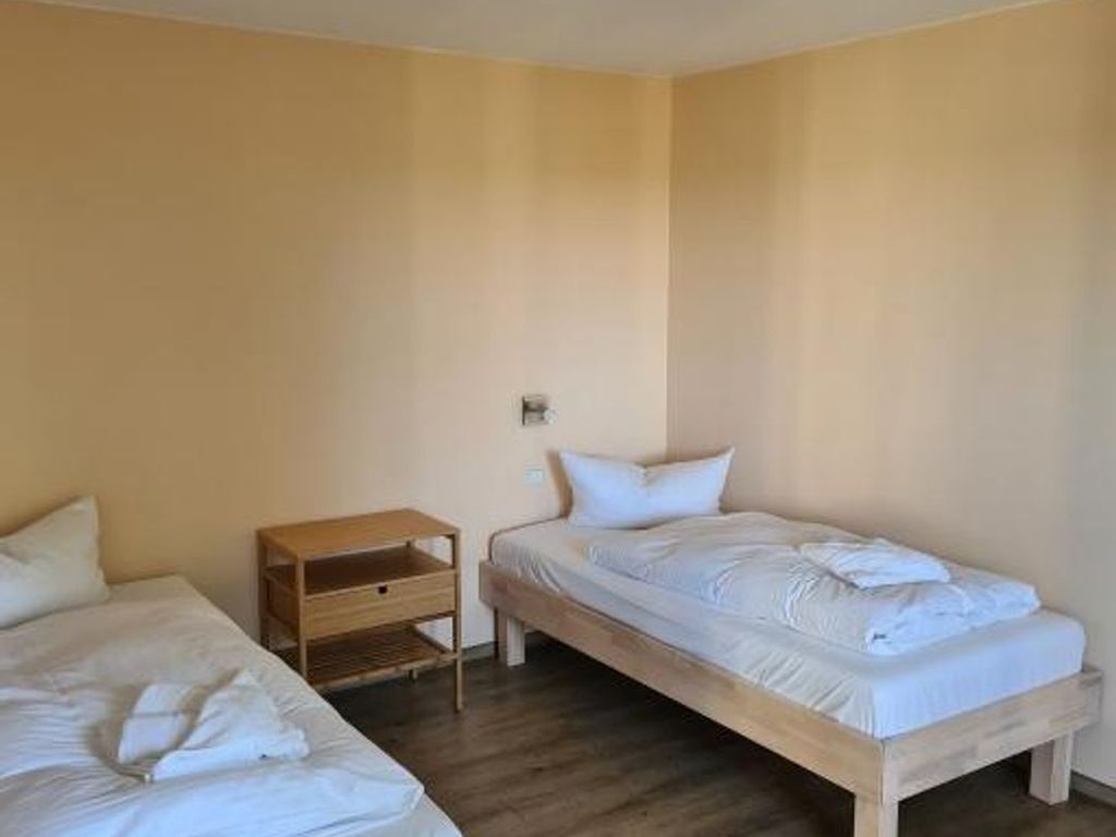 Ein Zimmer mit zwei Einzelbetten, einem Nachttisch aus Holz und einer Wandleuchte.