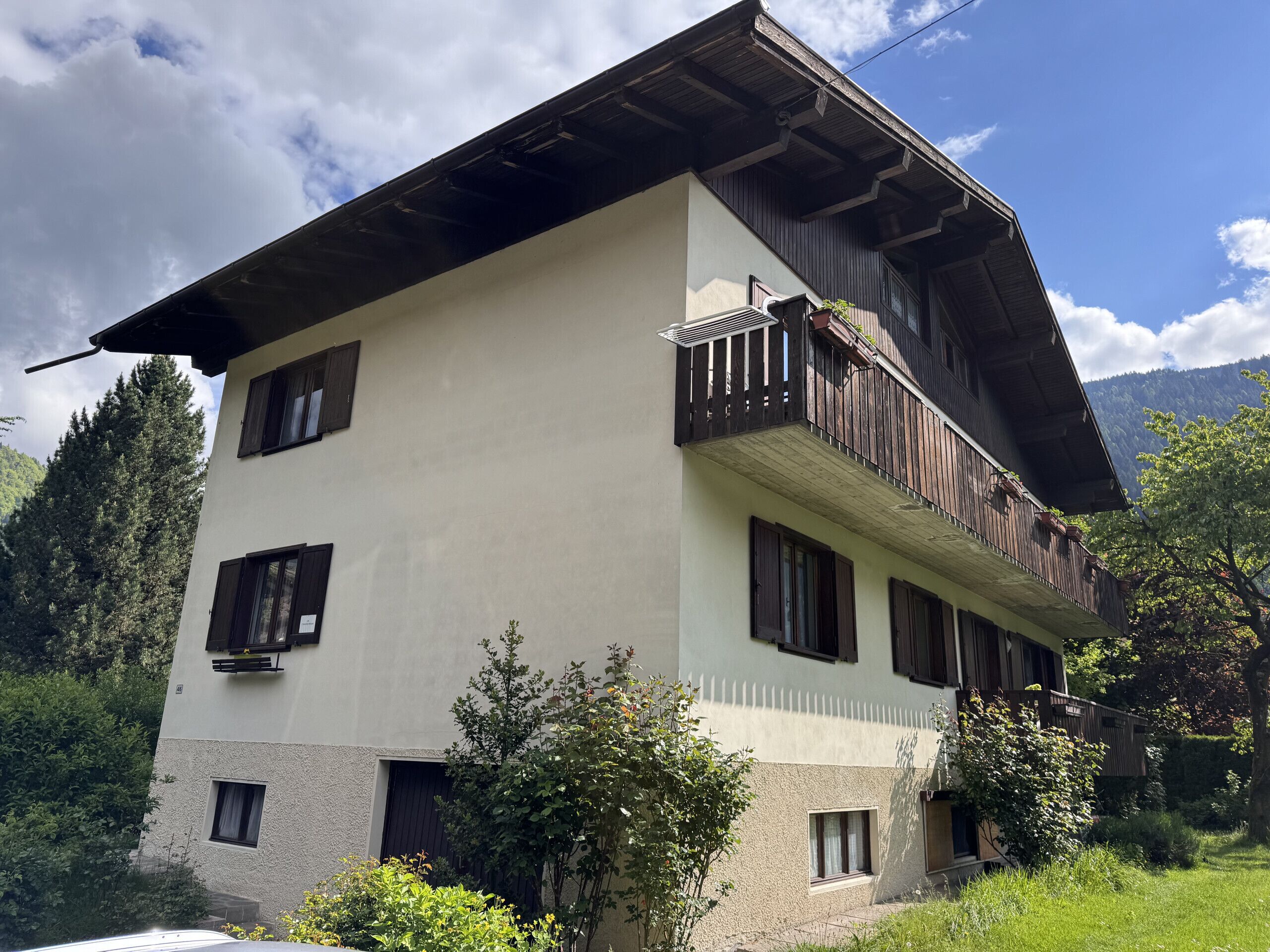 Un bâtiment à deux étages doté d’un balcon, entouré de verdure et de montagnes.