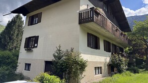 Ein zweistöckiges Gebäude mit Balkon, umgeben von Grünpflanzen und Bergen.